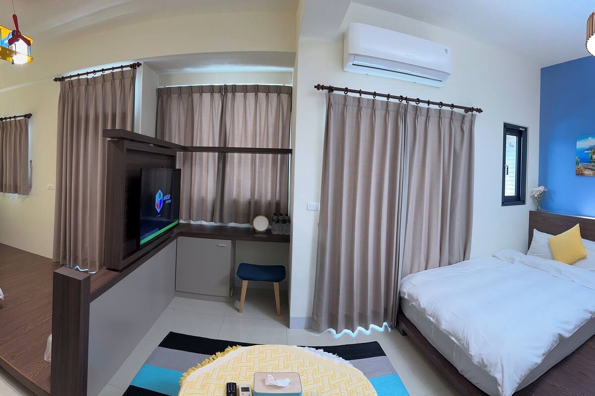 Ein Hotelzimmer mit zwei Betten, einem Fernseher, einem Schreibtisch und einer Klimaanlage.