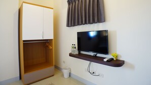 Une chambre dotée d’une armoire, d’un téléviseur à écran plat, d’une étagère avec des bouteilles et une télécommande, ainsi que d’un climatiseur fixé au mur.