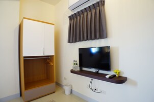 Una habitación con armario, televisión de pantalla plana, estante con botellas y un mando a distancia, y aire acondicionado instalado en la pared.
