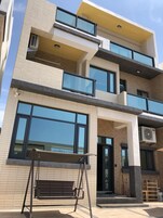 Un edificio de varios pisos con grandes ventanales, un columpio y una puerta con un escalón que conduce a la entrada.
