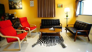 Un salon comprenant un canapé, deux fauteuils, une table basse, un tapis à motifs zébrés, un tableau, une horloge, une lampe et une fenêtre.