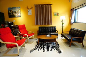 Una sala de estar con un sofá, dos sillones, una mesa de centro, un felpudo de cebra, un cuadro, un reloj, una lámpara y una ventana.