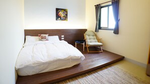 Une chambre à coucher avec un lit, une chaise, une petite table, un tableau et une fenêtre avec des rideaux.