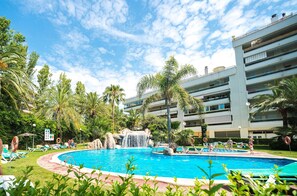 Uma área de piscina com cachoeira, cercada por palmeiras e espreguiçadeiras.
