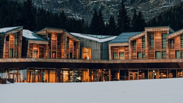 Een modern verblijf met meerdere houten hutten, gelegen voor een besneeuwde berg.