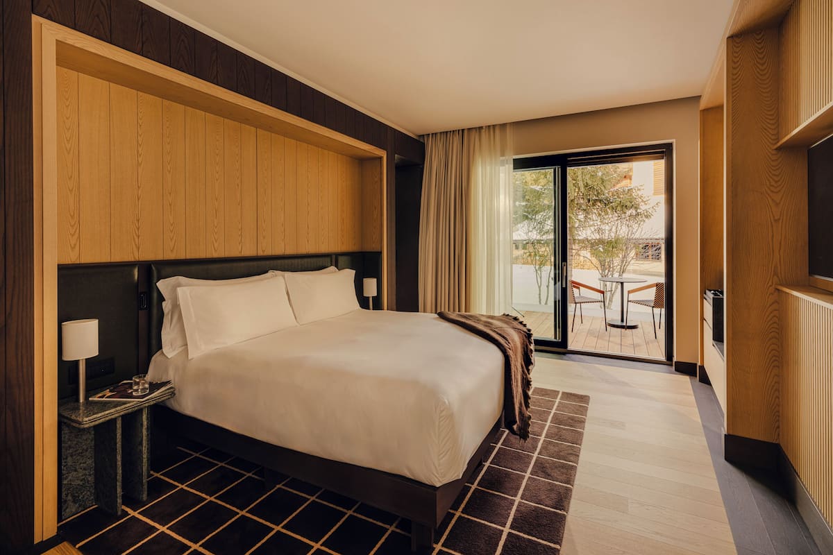 Habitación de hotel con una cama grande, una mesita de noche, una lámpara y vistas al patio exterior.