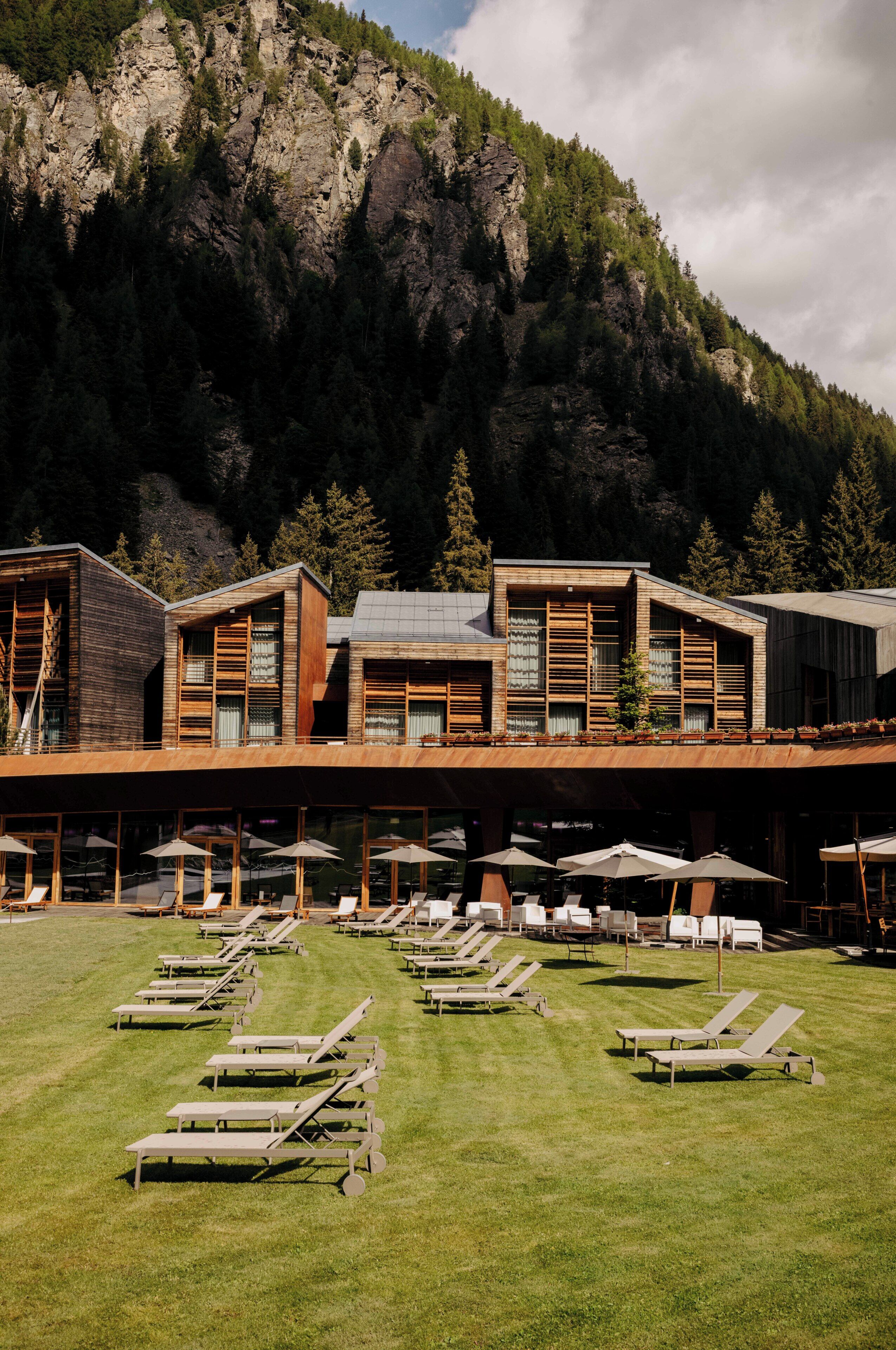 Un hotel con le montagne sullo sfondo, poltrone da esterno e una zona patio coperta.