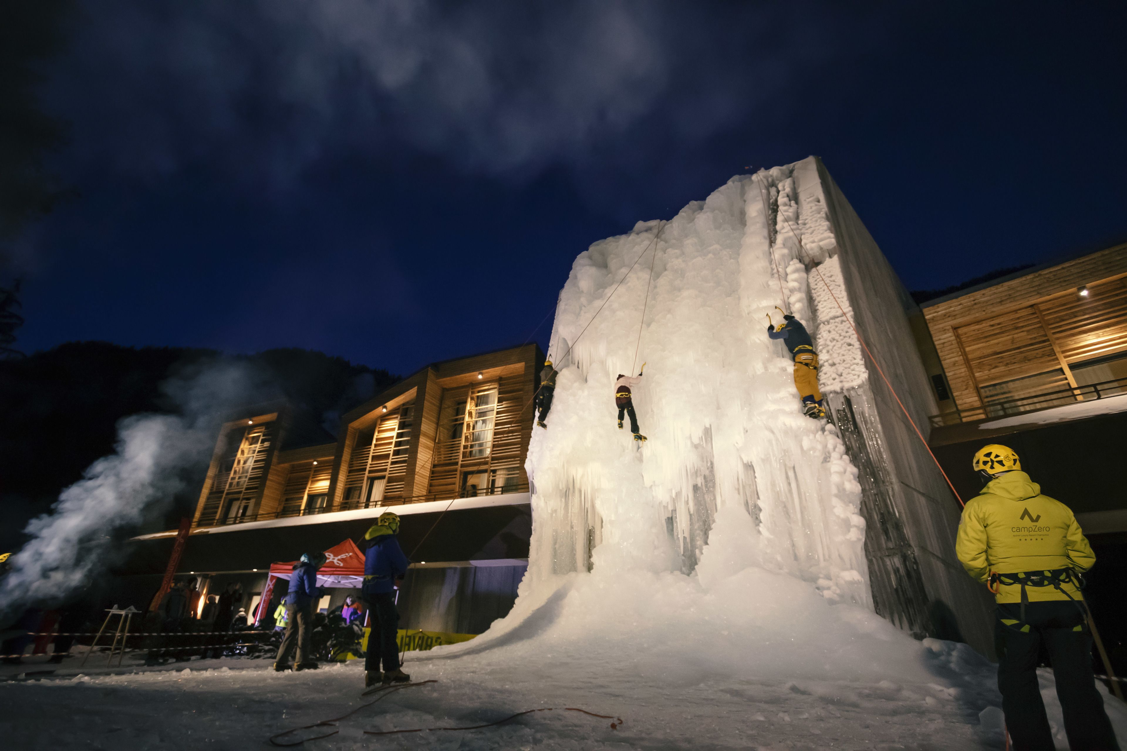 Una gran estructura de hielo con gente escalando y esquiando, rodeada de edificios.