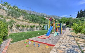 Ein Spielplatz mit Rutsche und Klettergerüsten, umgeben von einer Steinmauer und viel Grün.