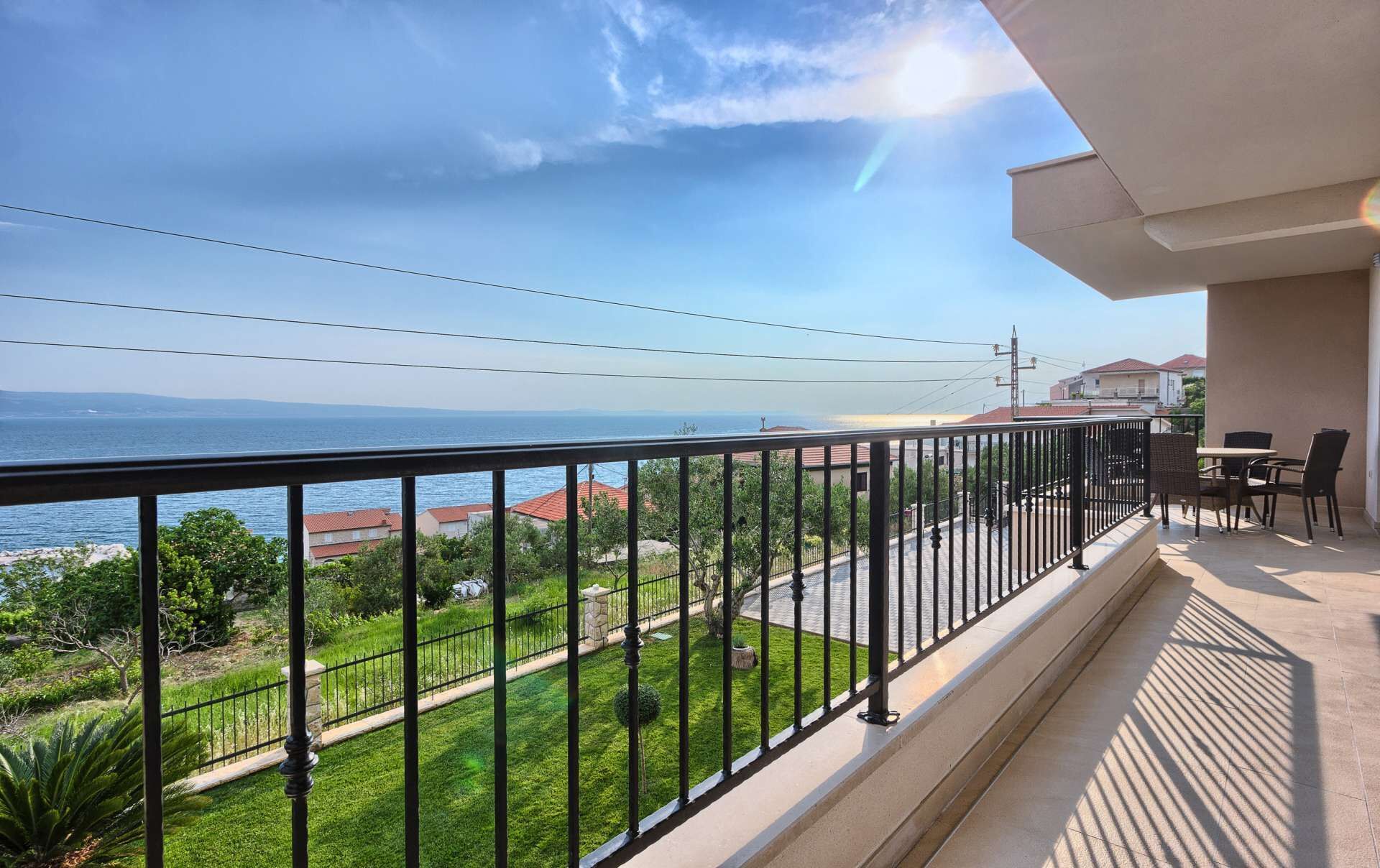 Ein Balkon mit Meerblick, eine Rasenfläche und eine Essbereich mit Stühlen und Tischen.