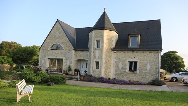 A stone house with a steeply pitched roof, a central tower, and a front porch with potted plants. - Chambre d'hôtes Mon Taj Mahal (Gueron)