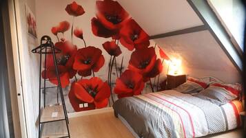 A bedroom with a bed, a hanging light fixture, and a wall with poppy flower artwork.