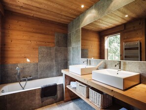 Une salle de bain moderne avec un plafond en bois, deux lavabos, une baignoire et un grand miroir.
