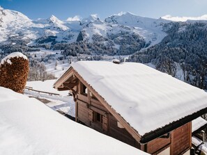 Een houten hut met een met sneeuw bedekte dak, omgeven door een bergachtig landschap.