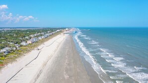 Une vue sur la côte, avec une longue plage de sable, une jetée qui s’avance dans l’eau et une rangée de maisons le long du rivage.