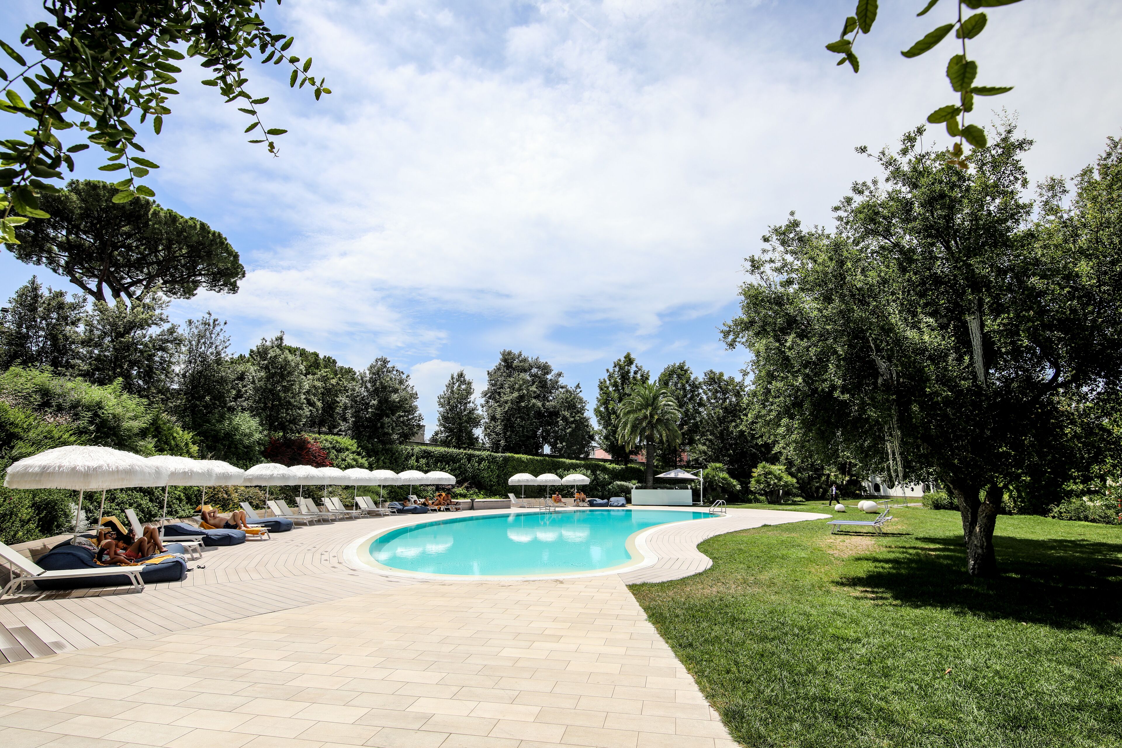 A swimming pool with lounge chairs and umbrellas, surrounded by greenery and trees.