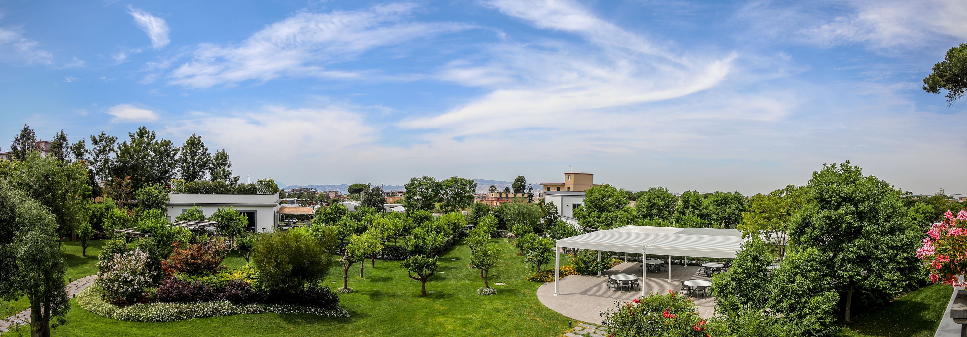 Un exuberante jardín con un pabellón, un porche cubierto y vistas a edificios lejanos.