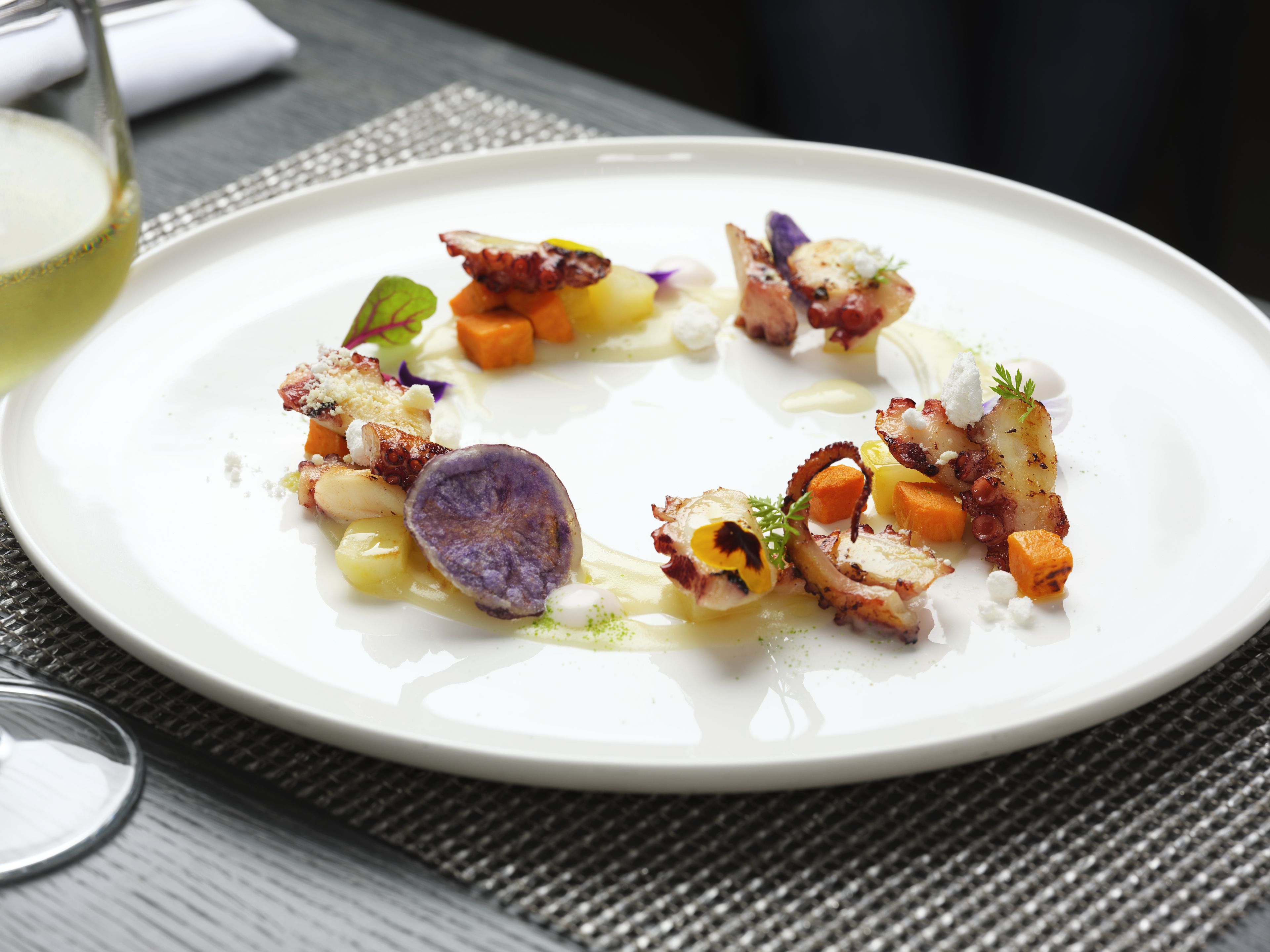 A white plate with a variety of food items, including octopus, vegetables, and a dollop of cream.