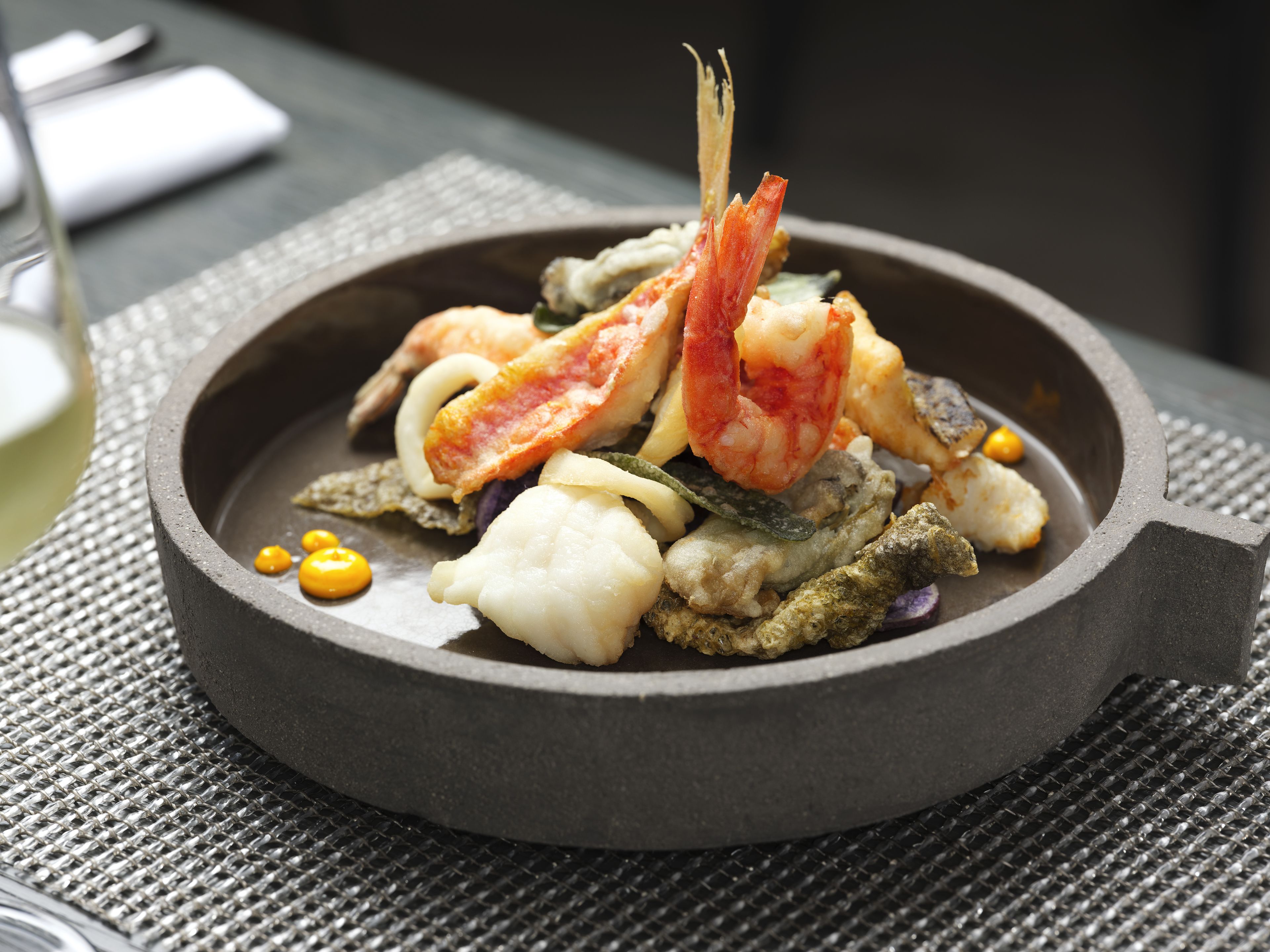 A seafood dish in a round, dark-colored bowl on a textured surface.