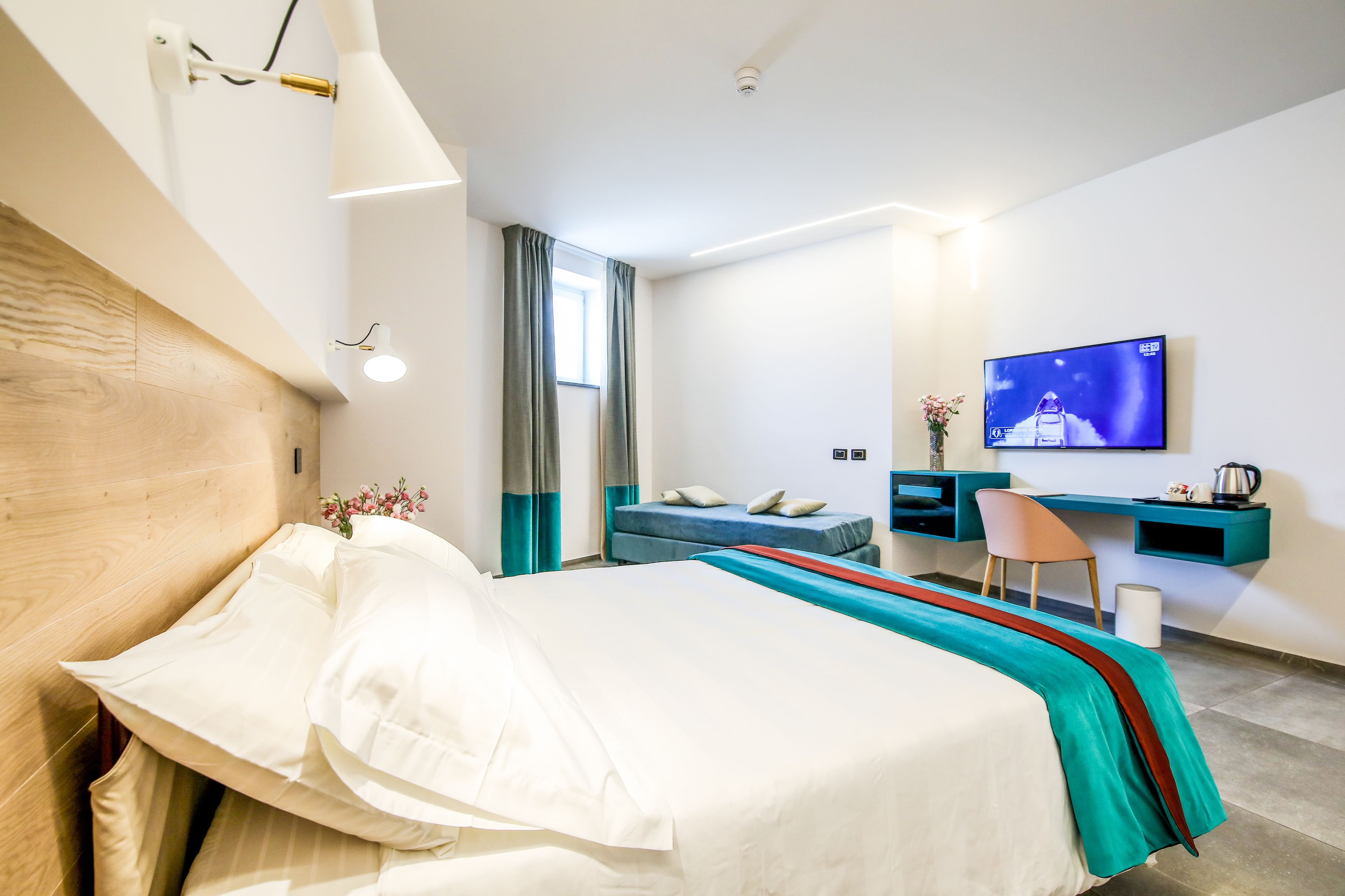Una moderna camera d'albergo con un letto rifatto, una scrivania con sedia, una televisione e una finestra con tende.