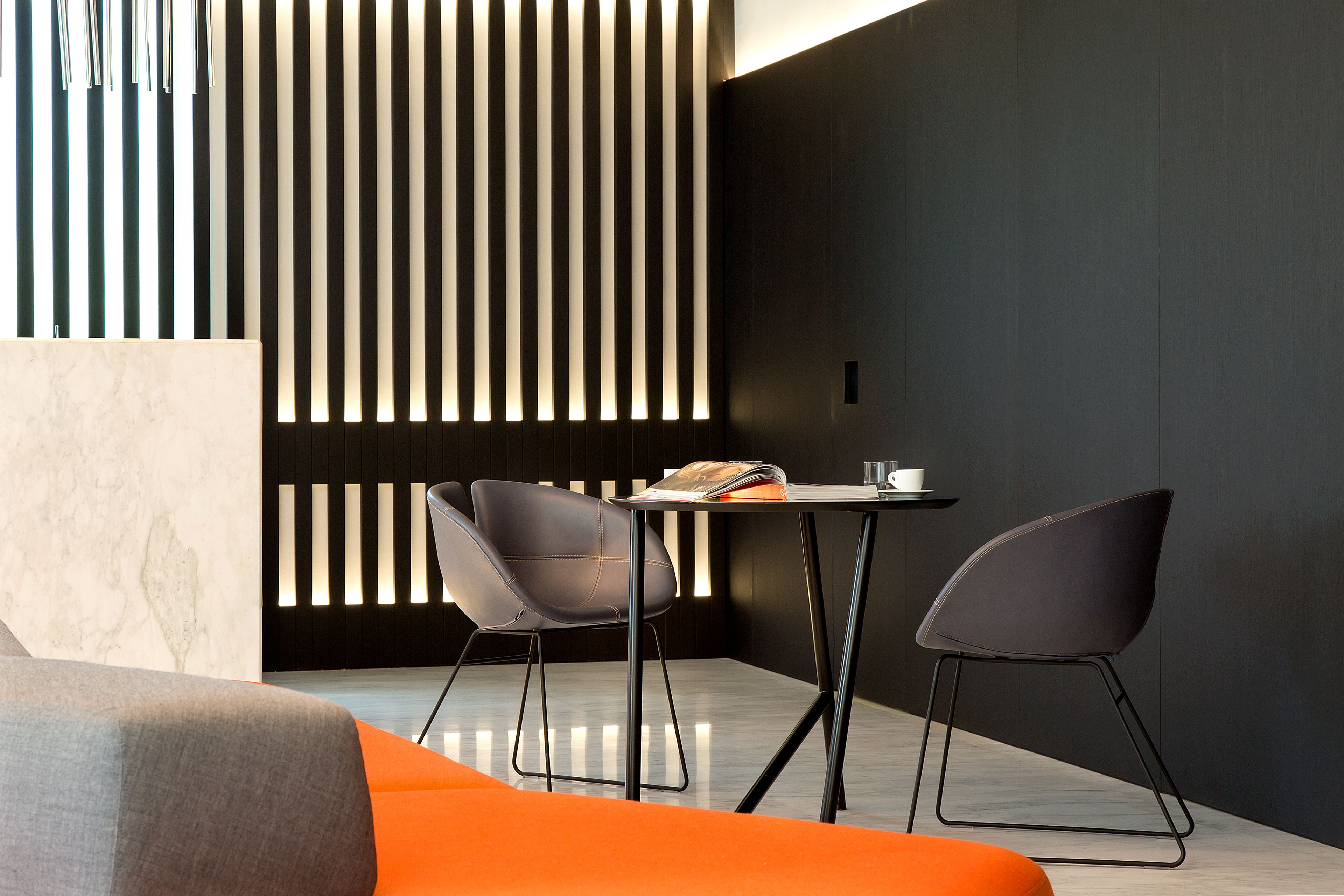 Ein modernes Interieur mit dunkler Wand, hellem Boden und zwei Stühlen um einen Tisch.