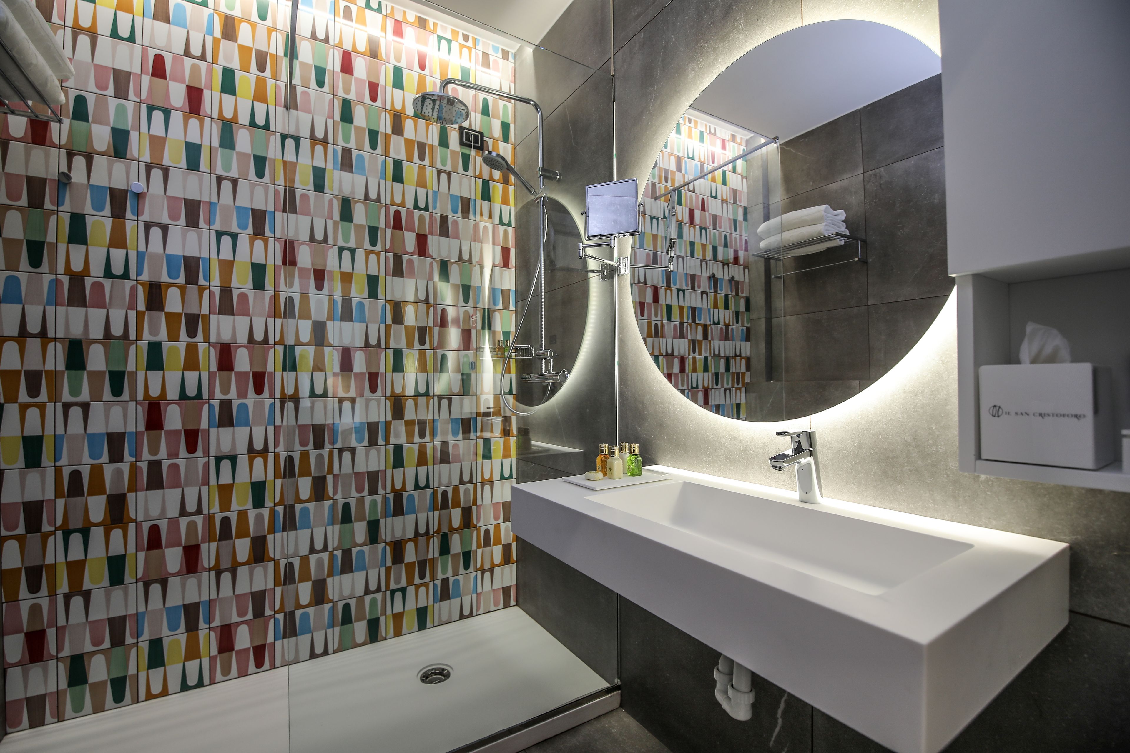 A modern bathroom with a colorful tile wall, a white sink, and a shower.