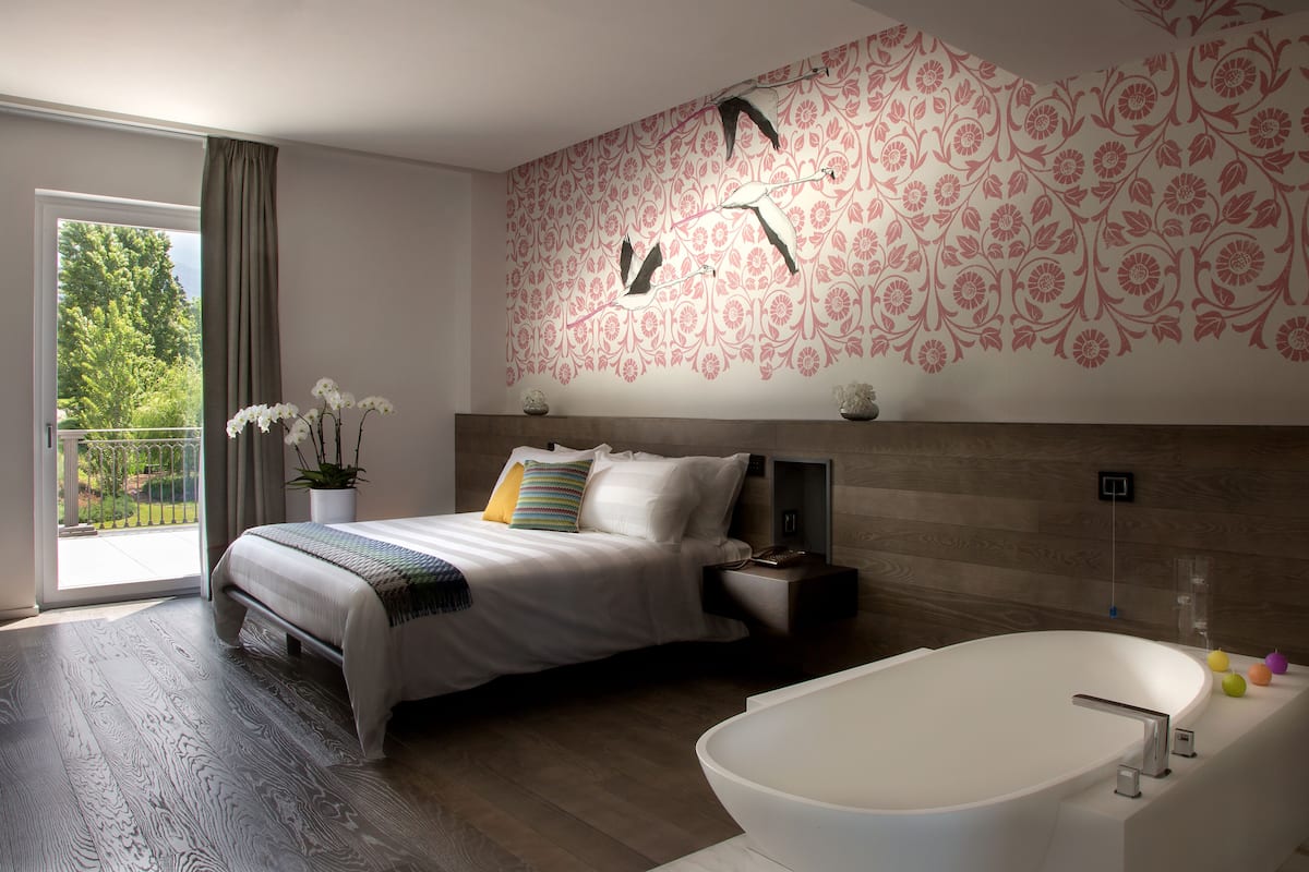 A modern bedroom with a large bed, a bathtub, and a balcony with a view of trees.
