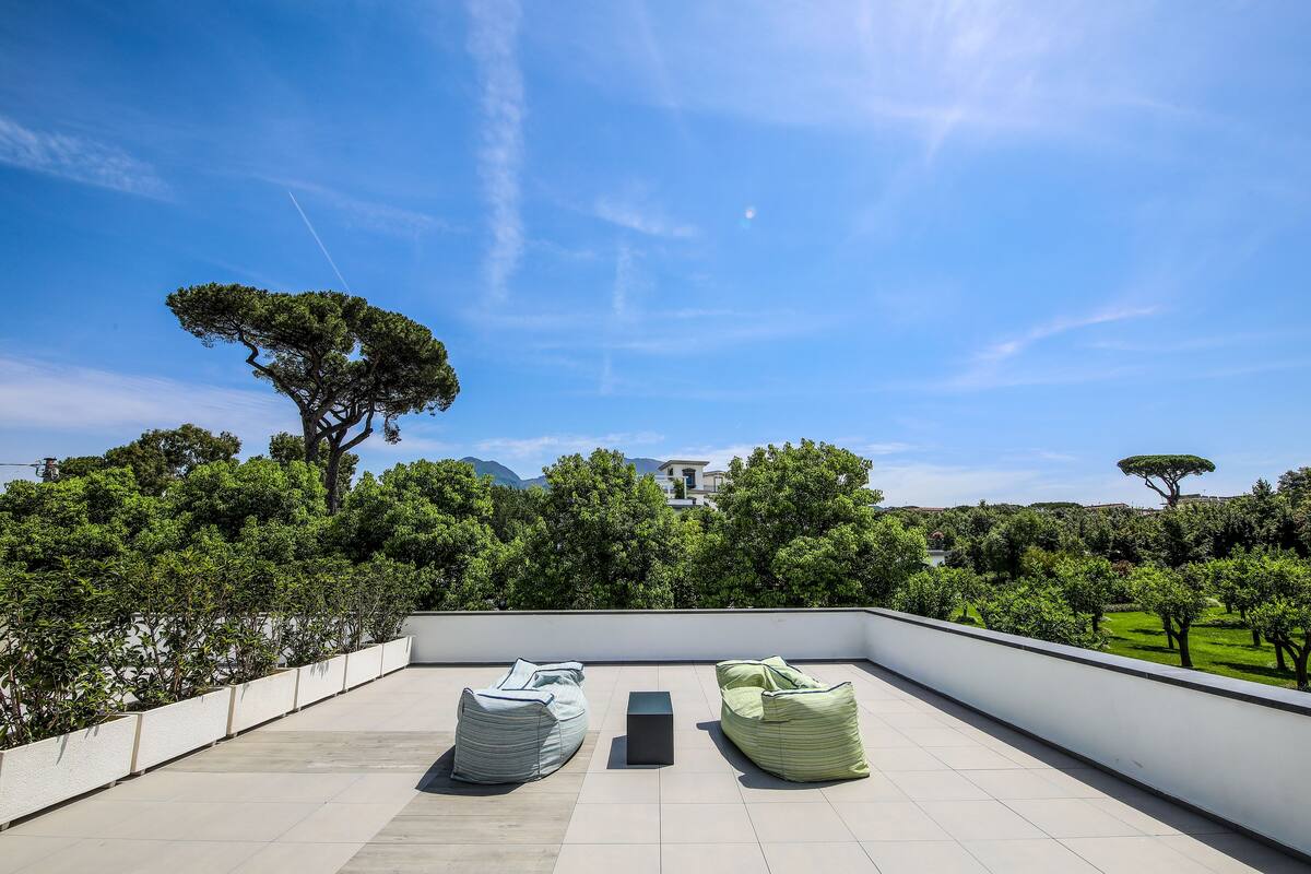 A rooftop terrace with two bean bags, a small table, and a view of a tree and distant building.