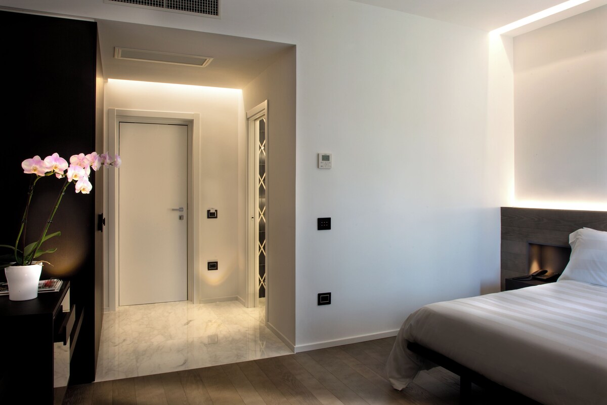 A modern hotel room with a bed, bedside table, and a potted orchid.