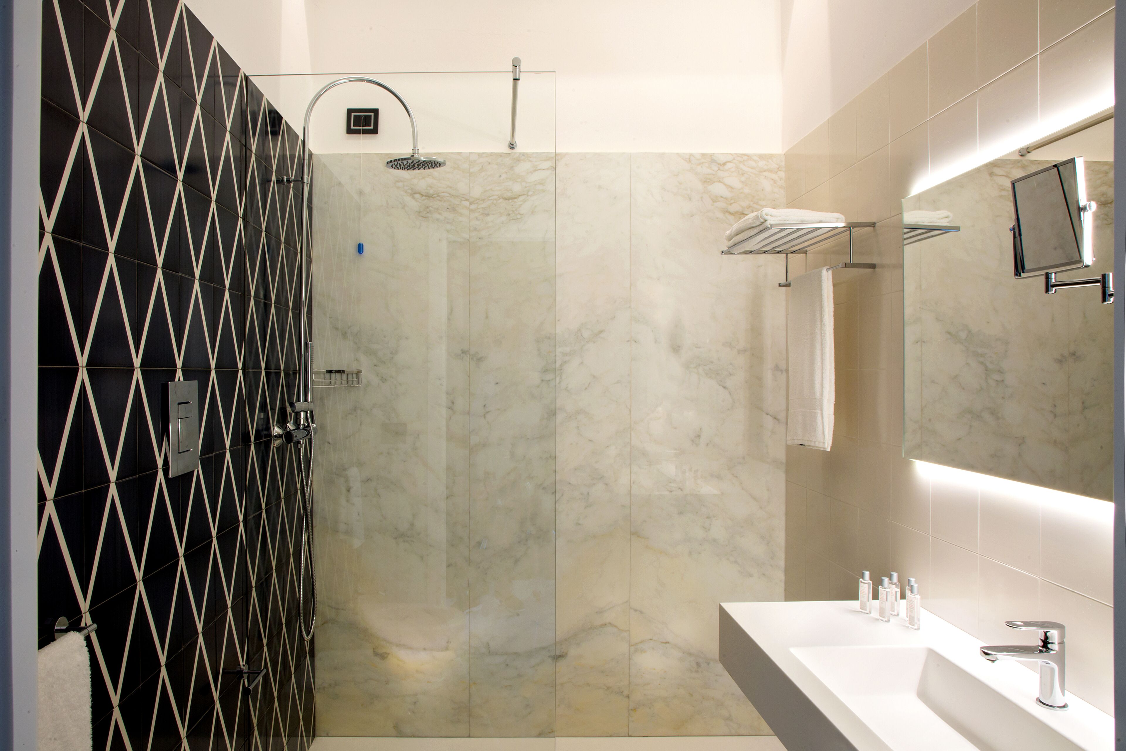 Un baño moderno con ducha de vidrio, paredes de mármol y lavamanos blanco con espejo.