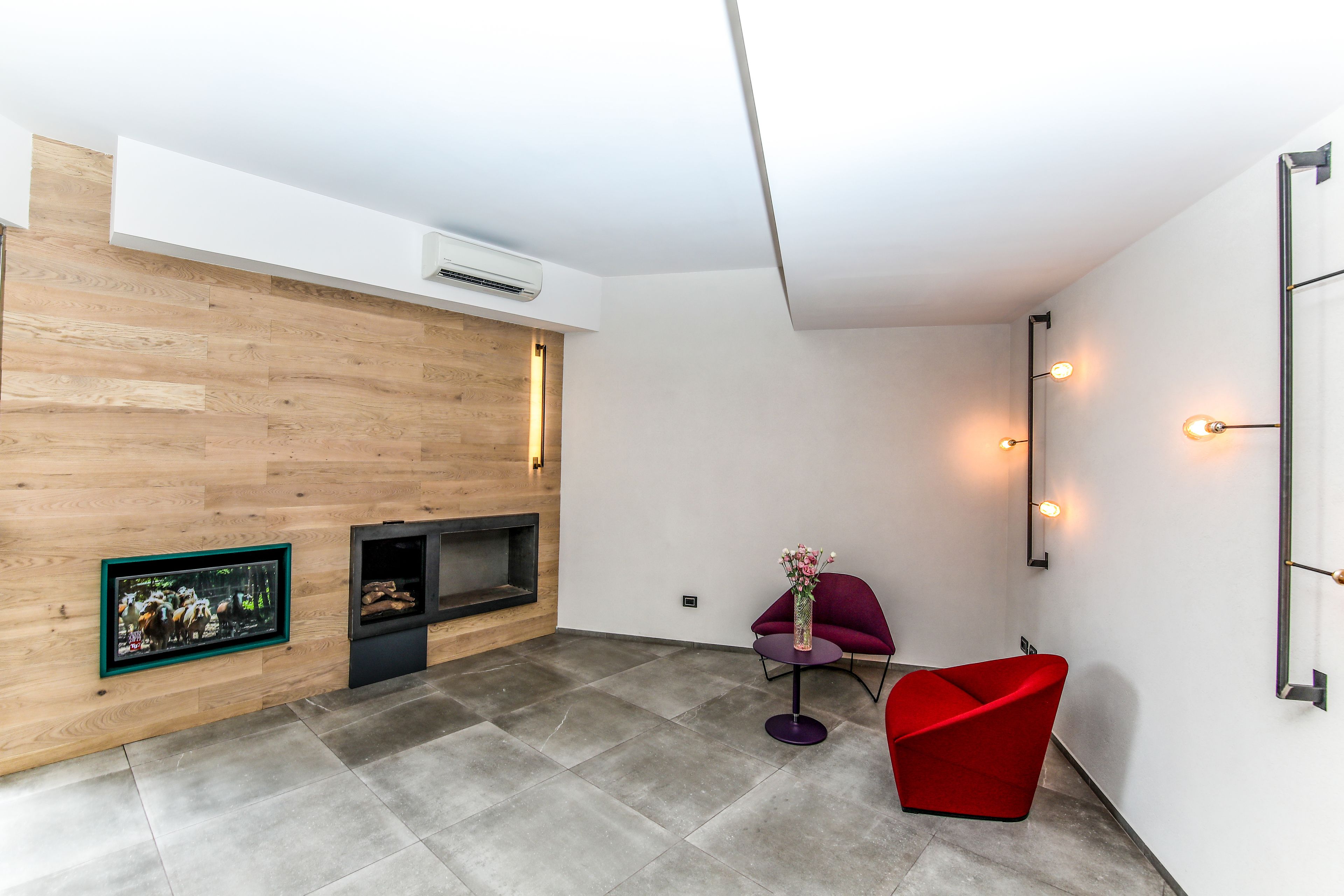 Ein modernes Wohnzimmer mit einer Holzvertäfelung, einem Kamin, einem roten Sessel und einem kleinen Tisch mit einer Vase.