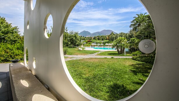 A view through a circular window of a pool area with a mountain backdrop. - Il San Cristoforo (Ercolano)