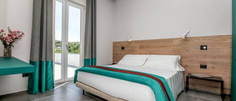 Une chambre moderne avec un grand lit, une tête de lit en bois, une table de chevet et une vue sur l’extérieur grâce à une porte-fenêtre coulissante.