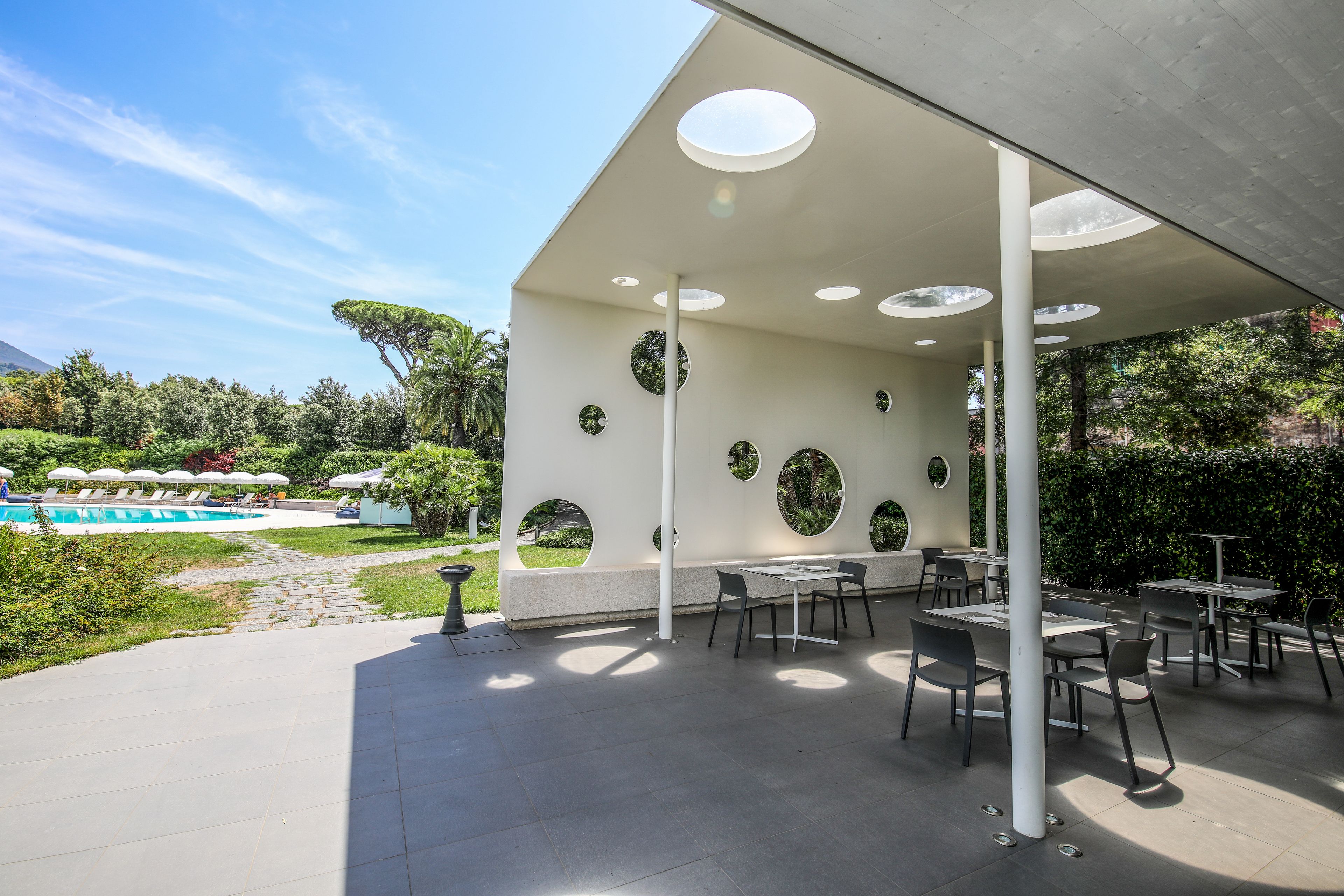 Un'area patio esterna con tavoli e sedie, una piscina e un giardino curato.