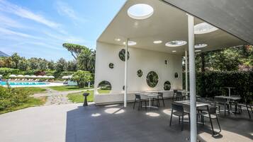 Un'area patio esterna con tavoli e sedie, una piscina e un giardino curato.