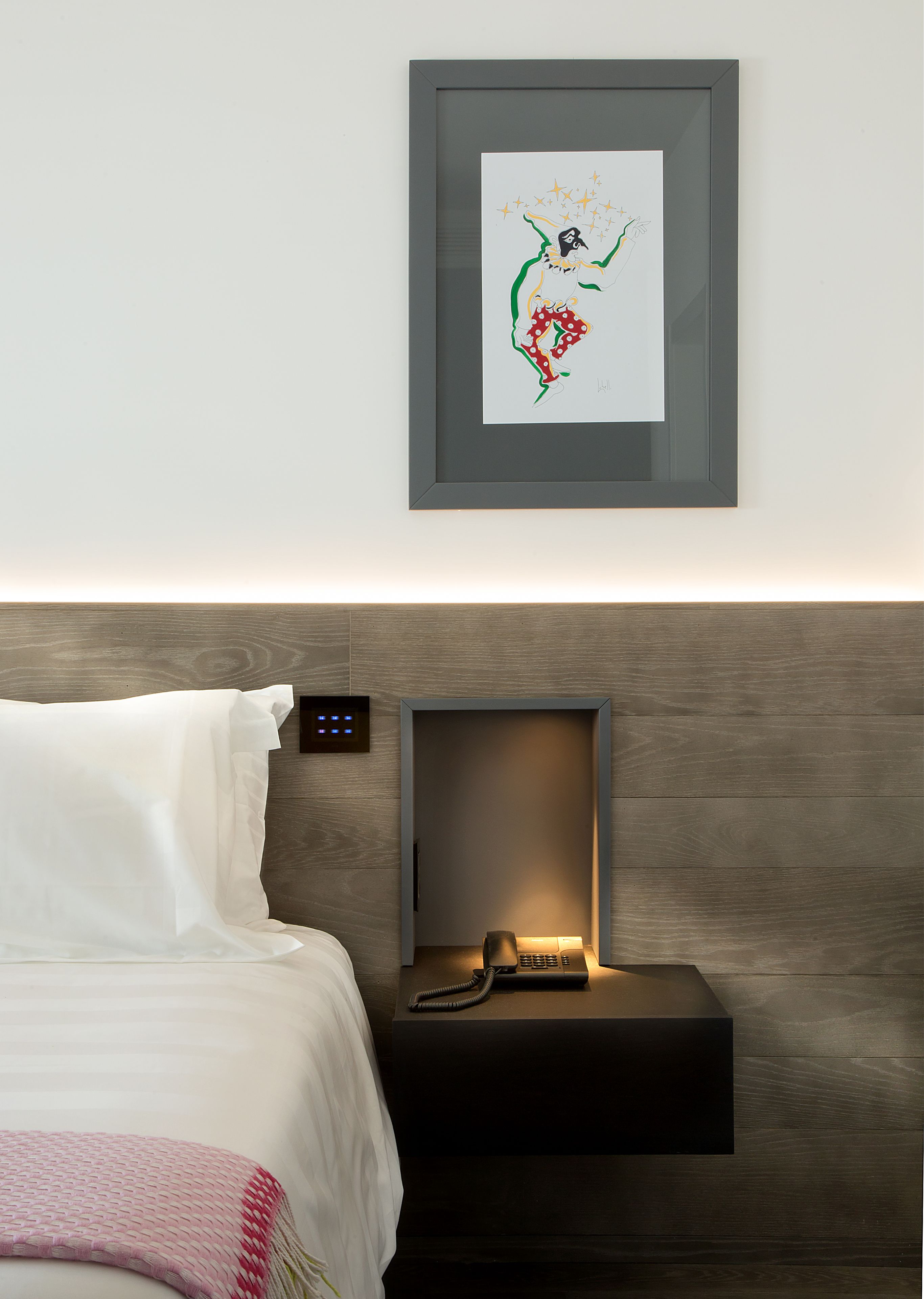 Ein ordentlich eingerichtetes Hotelzimmer mit einem Bett, einem Nachttisch mit Lampe und einem gerahmten Kunstwerk an der Wand.