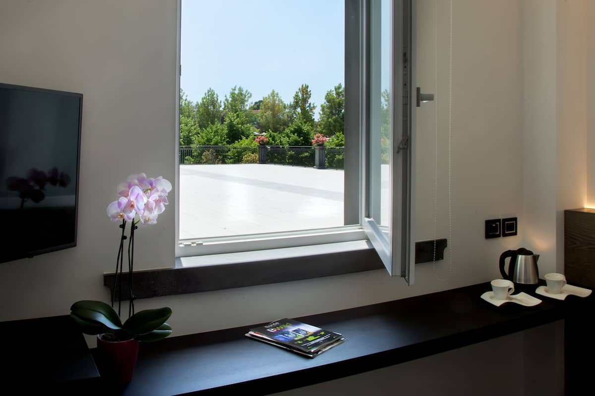 A modern room with a large window, a potted orchid, a magazine, two cups, and a kettle on a dark countertop.