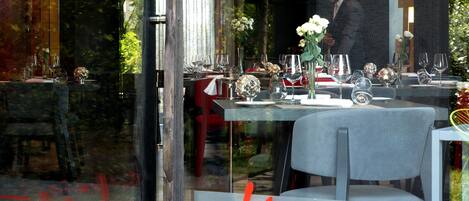 A restaurant with tables set for dining, a man in a suit standing in the background, and a window with the word "Line" written on it.
