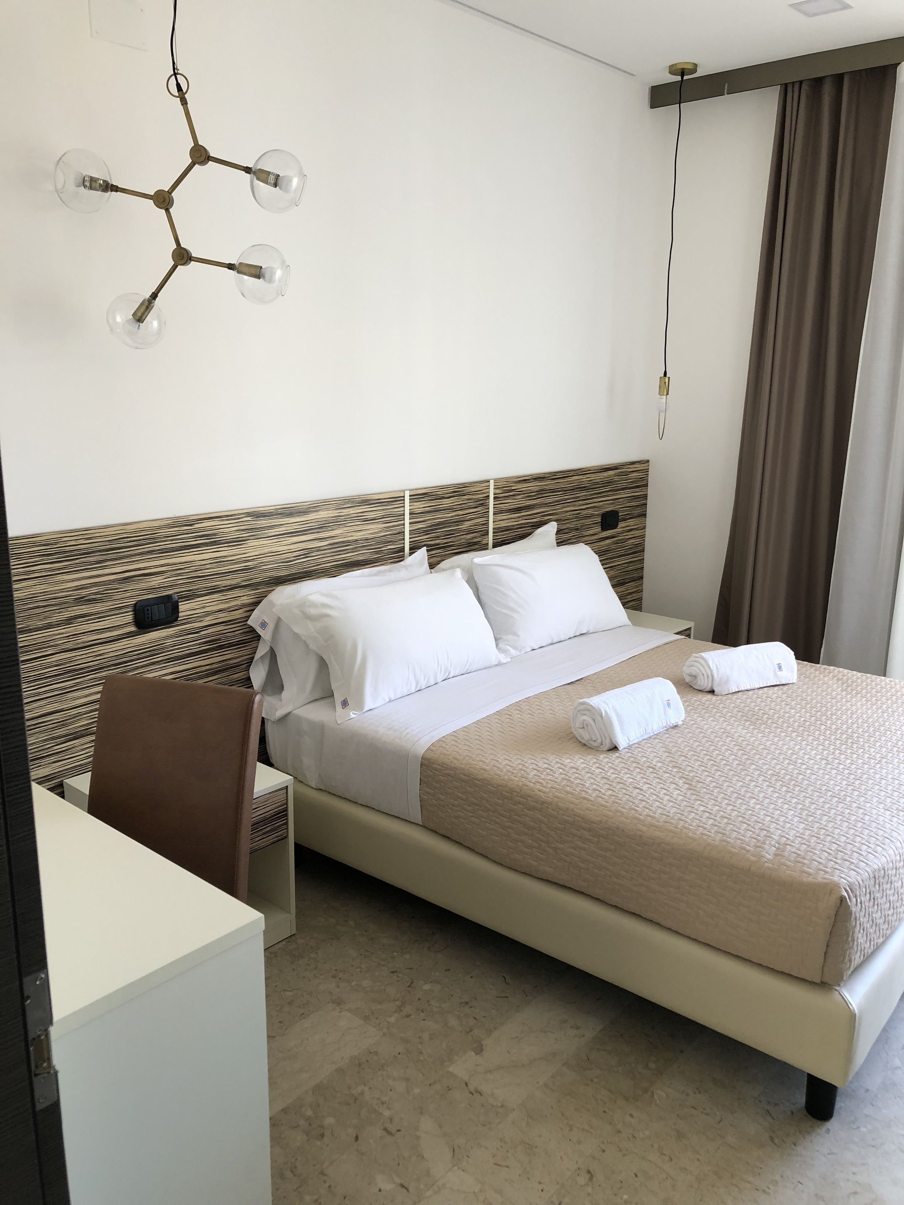 A hotel room with a bed, a desk, and a modern chandelier.
