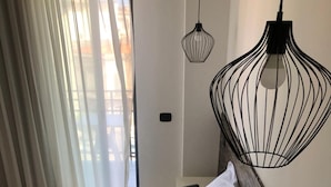 A hotel room with two beds, a large window with sheer curtains, a hanging black pendant light, and a small bedside table with a remote control. - Milazzo INN AiMori (Milazzo)