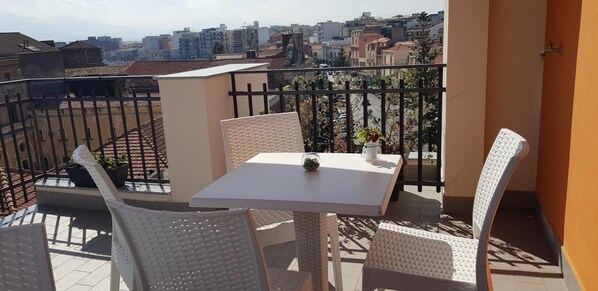 Uma varanda com mesa e cadeiras, vista para o horizonte urbano e um vaso de planta.