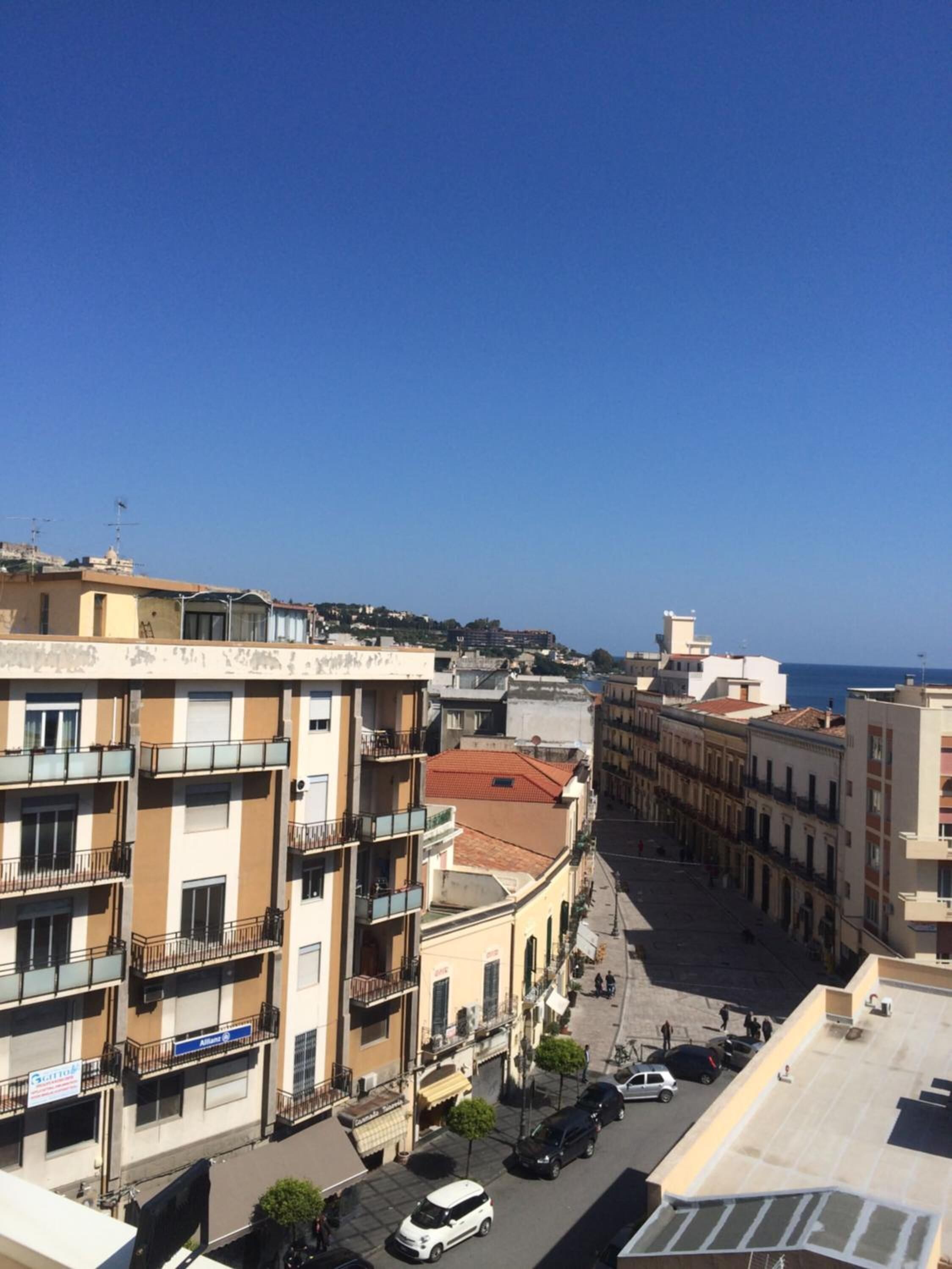 A cityscape with multi-story buildings, a clear sky, and a view of the sea.