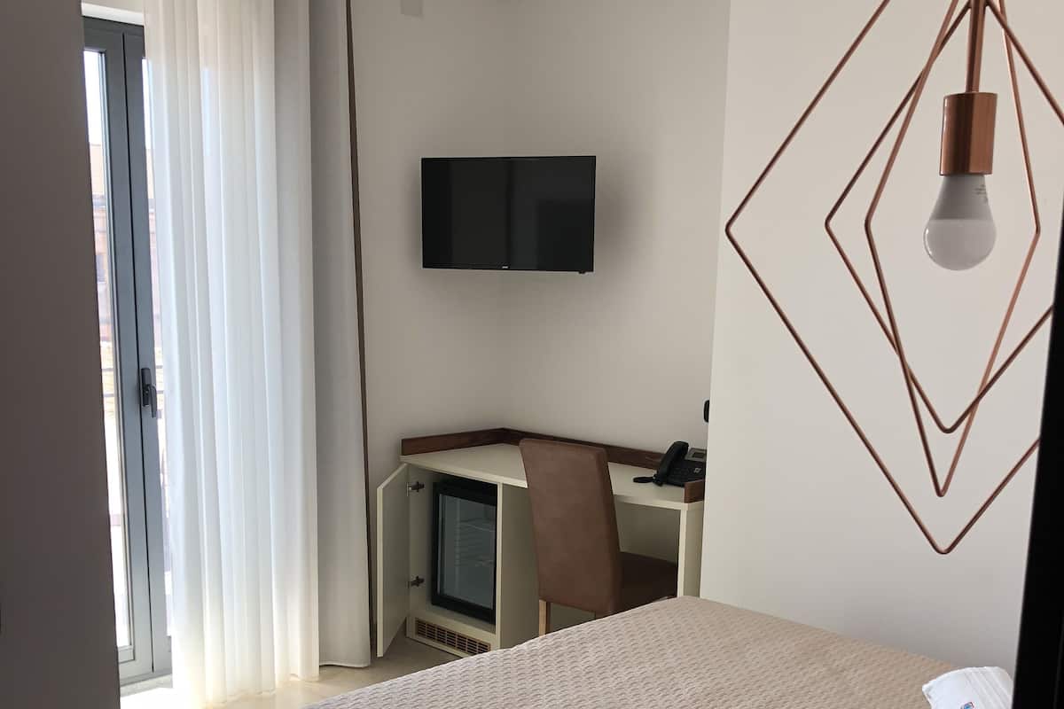 A hotel room with a bed, a desk with a chair, a television, and a window with curtains.