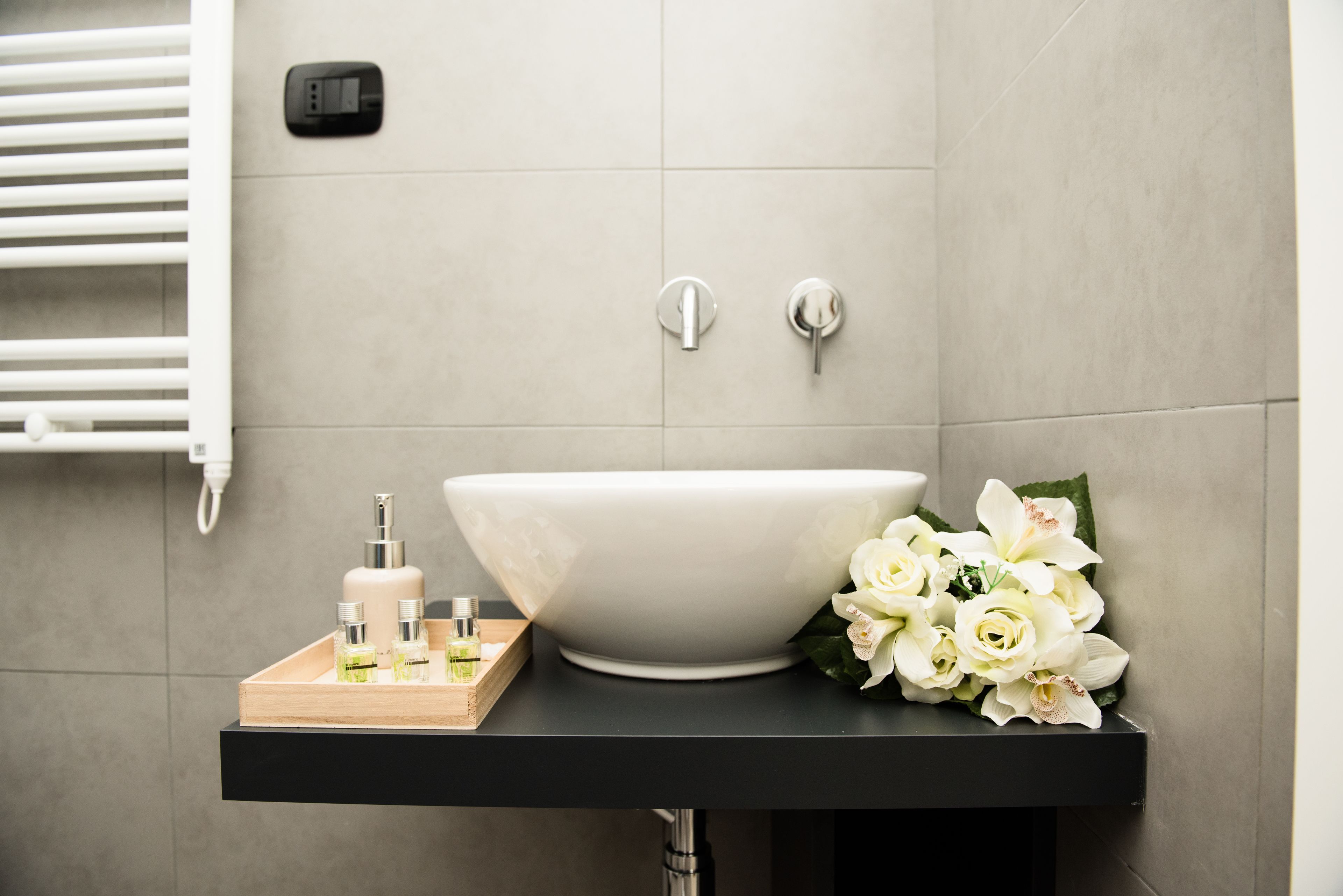 Ein modernes Badezimmer mit einem großen weißen Waschbecken, einer schwarzen Arbeitsplatte und einem Strauß weißer Blumen.
