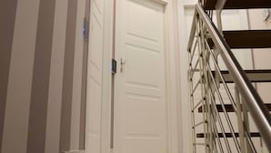 A white door with a keypad lock, a metal staircase with a handrail, and a wall with vertical stripes. - Milazzo INN AiMori (Milazzo)