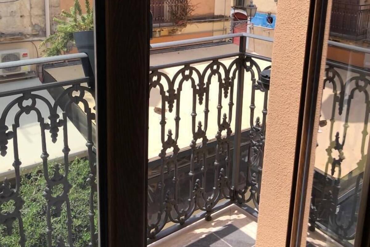A balcony with ornate metal railings, a tiled floor, and a view of neighboring buildings.