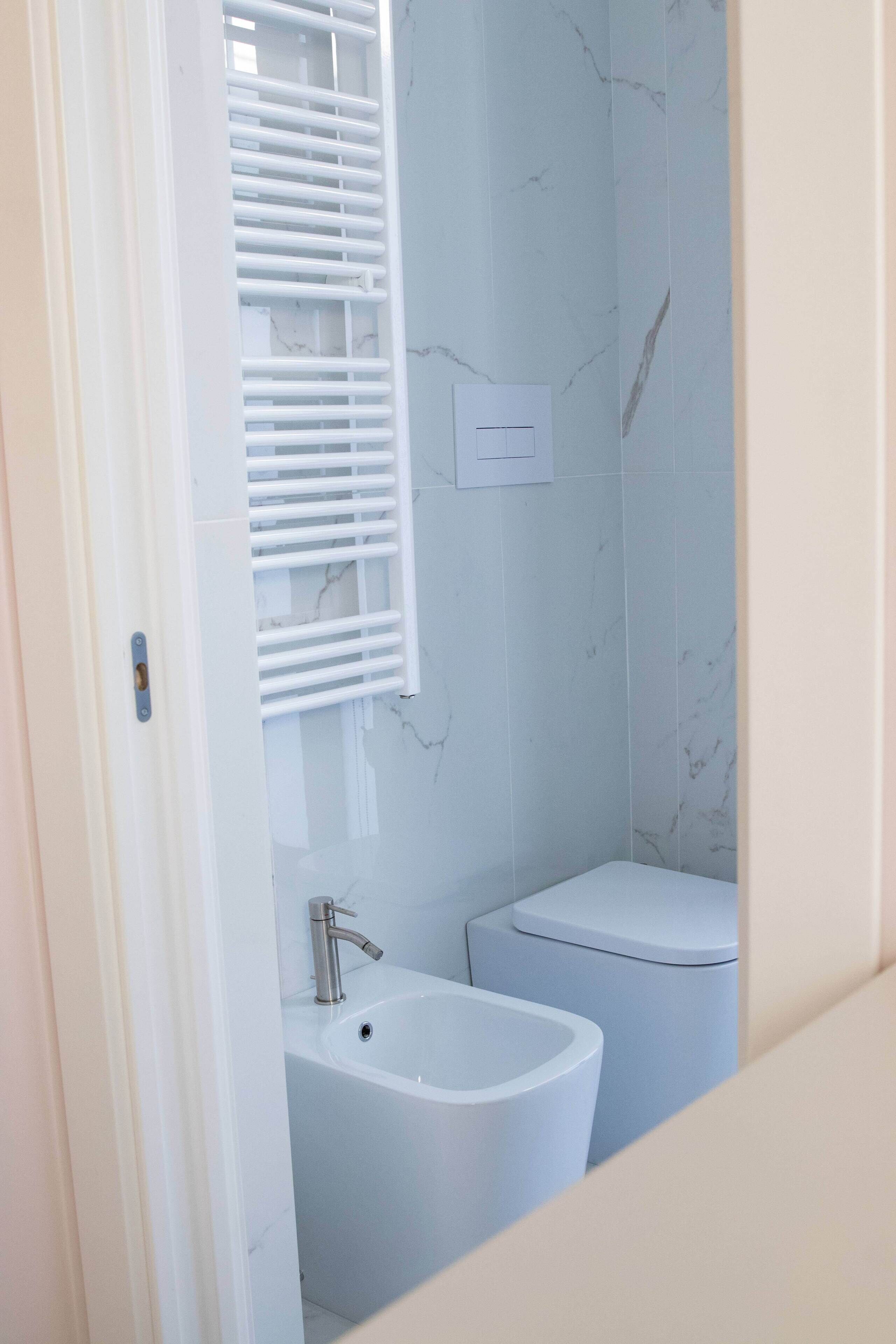 A bathroom with a white bathtub, a toilet, and a window with white blinds.