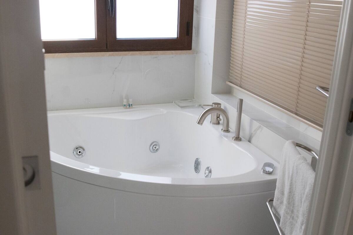 A modern bathroom with a freestanding bathtub, a vanity with a mirror, and a window with blinds.