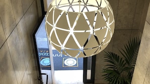 A modern interior with a geometric light fixture, tiled walls, and a visible logo on the floor. - Milazzo INN AiMori (Milazzo)