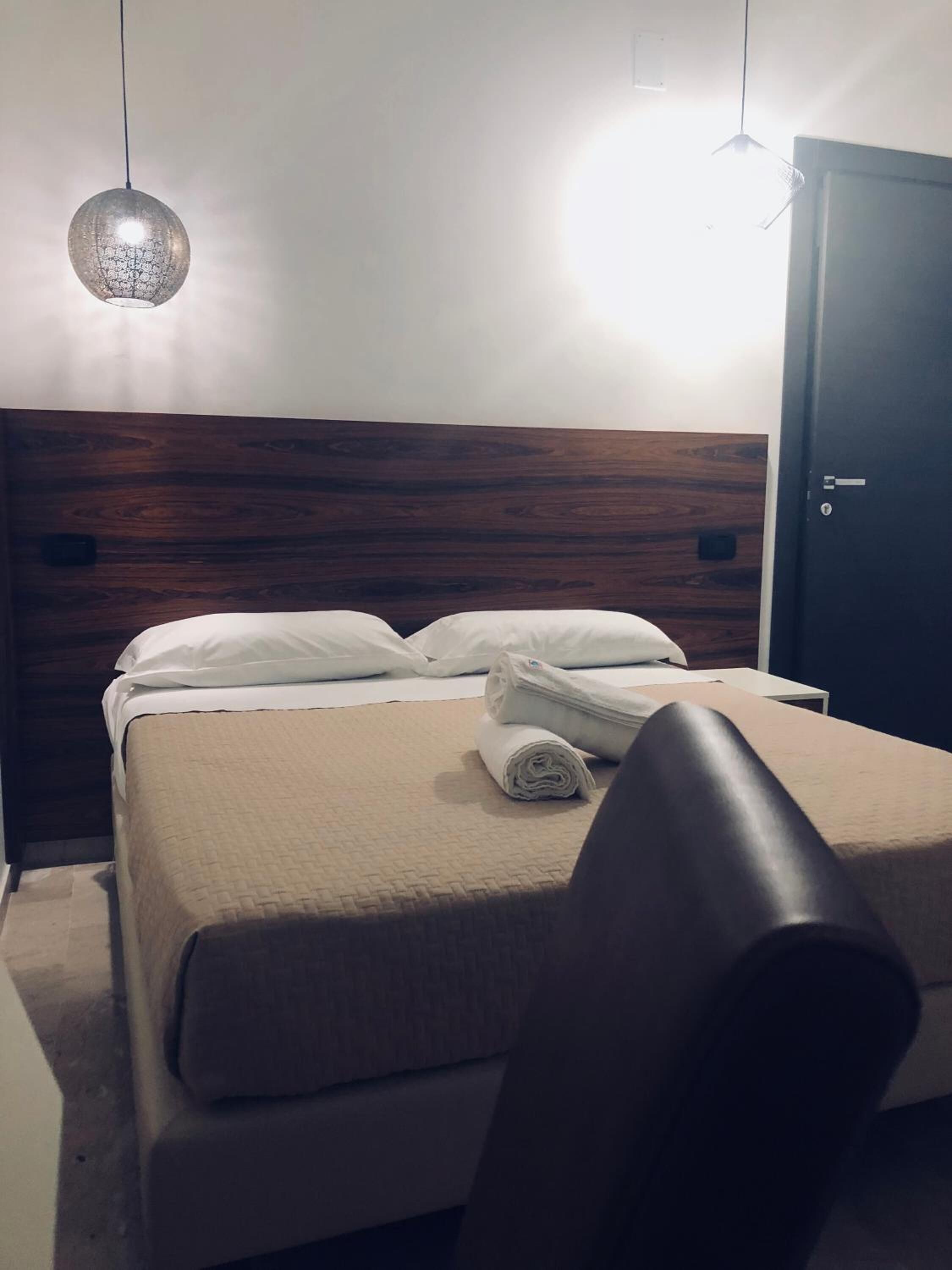 A neatly made bed with a beige bedspread and white pillows, a rolled towel, and a dark wooden headboard.